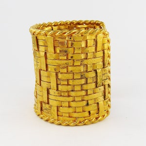 May include: A gold-toned woven bangle bracelet with a rope-like design around the edges.