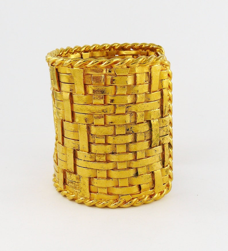 May include: A gold-toned woven bangle bracelet with a rope-like design around the edges.