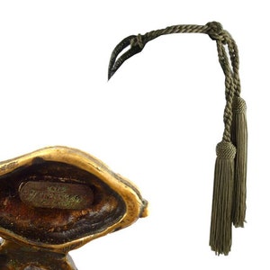 Puede incluir: Una escultura de bronce de un p&aacute;jaro con un cord&oacute;n de borlas verde. La escultura est&aacute; firmada "1978 Bruno Zacharias" en la parte inferior.