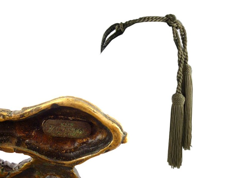 Puede incluir: Una escultura de bronce de un p&aacute;jaro con un cord&oacute;n de borlas verde. La escultura est&aacute; firmada "1978 Bruno Zacharias" en la parte inferior.