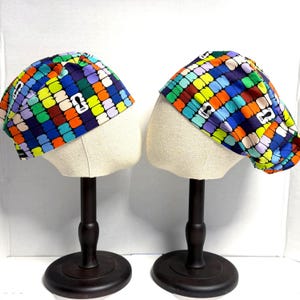 May include: Two scrub caps featuring a repeating grid pattern of colorful rounded squares in shades of blue, green, orange, yellow, and purple. Each cap displays a small white rectangular logo with the text FIFA printed in black lettering.