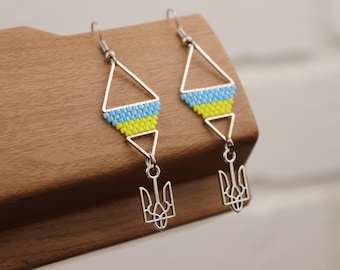 Puede incluir: Un par de pendientes de plata con un diseño de triángulo de cuentas azules y amarillas y un dije de tridente de plata.