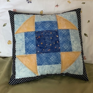 May include: A square cushion with a patchwork design featuring blue and yellow fabric. The cushion has a black and white polka dot border.