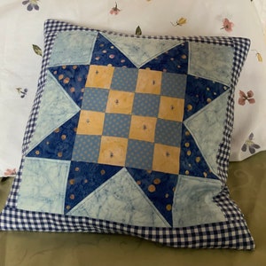 May include: A blue and yellow patchwork cushion with a star design and a gingham border.