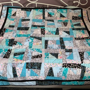 May include: A patchwork quilt with a black border. The quilt is made of various fabrics in shades of blue, grey, and white with floral patterns.