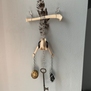 May include: A bone mobile with a feather, a key, a locket, and a black stone hanging from it.