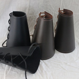 May include: Three leather arm guards with laces. Two are brown and one is black.
