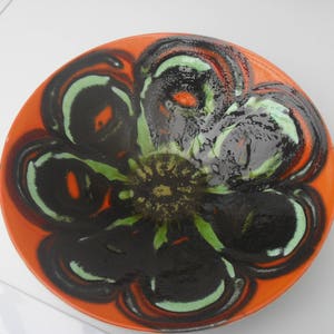 May include: A large, round ceramic bowl with a bright orange background and a black and green floral design. The bowl has a glossy finish.
