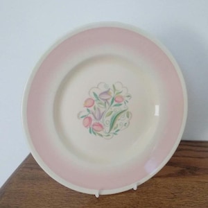 Könnte beinhalten: Ein weißer Keramikteller mit rosa Rand und einem floralen Design in der Mitte. Die Blumen sind rosa, lila und grün.