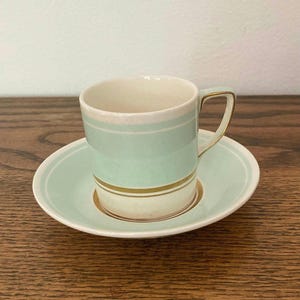 May include: A light green and gold striped teacup and saucer set. The cup has a white interior and a gold rim. The saucer has a light green rim.