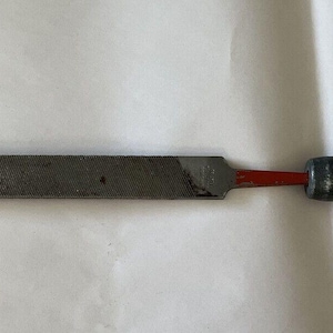 May include: A metal file with a wooden handle. The file has a red painted tip and a rough surface. The handle is made of light brown wood.