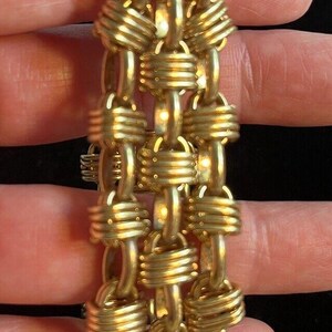 May include: A gold-toned chain bracelet with a woven design. The bracelet is made of multiple strands of chain that are woven together to create a textured look.
