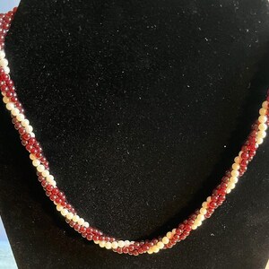 May include: A twisted necklace made of small red and white beads.