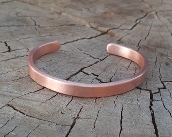 May include: A simple copper bracelet with a brushed finish. The bracelet is open and has a rounded shape.