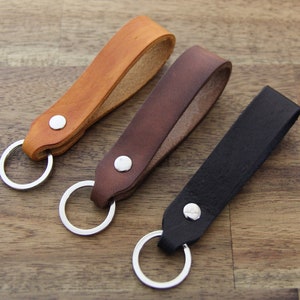 May include: Three leather keyrings with silver key rings. The keychains are brown, dark brown, and black.
