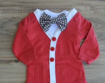 May include: Red baby bodysuit with a white collar and trim, featuring three red buttons down the front. A green and pink patterned bow tie is attached. The bodysuit is designed to resemble a suit jacket.