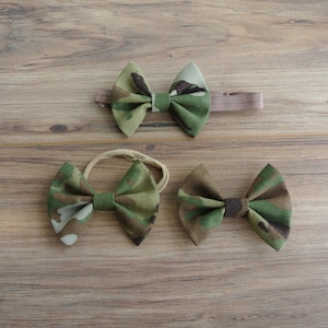 May include: Three camouflage patterned fabric bow headbands. The bows are tied in a classic bow shape. The headbands are made of elastic.