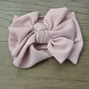 Peut inclure: Un bandeau en tissu rose poussiéreux avec un grand nœud noué. Le bandeau est fait d'un tissu texturé.