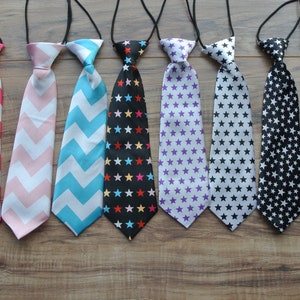 May include: Eight different patterned neckties for kids. The ties are made of fabric and have a variety of colors and patterns, including pink and white chevron, blue and white chevron, black and white stars, and purple and white stars.