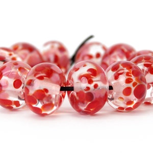 以下が含まれることがあります： 赤い斑点模様の赤と白のガラスビーズのネックレス。ビーズは黒い紐に通されています。