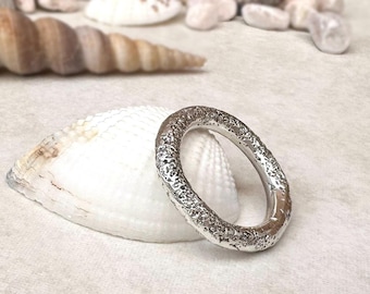 May include: A silver ring with a textured, rough, and uneven surface finish. The band has a circular shape and a metallic luster, displaying a granular, pitted appearance across its entire outer circumference, contrasting with a smooth inner edge.