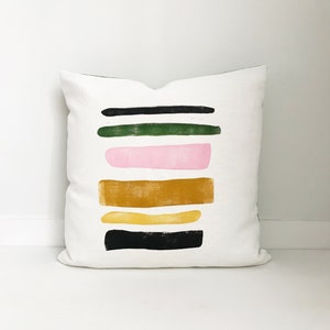 May include: White pillow with a geometric design featuring black, green, pink, and yellow stripes.
