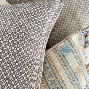 May include: Three decorative throw pillows with geometric patterns. The pillows are made of woven fabric with a textured surface. The pillows are in shades of gray, brown, and blue.