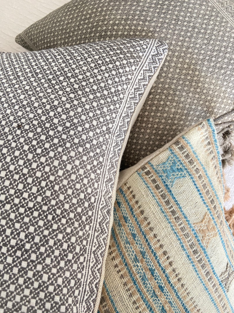 May include: Three decorative throw pillows with geometric patterns. The pillows are made of woven fabric with a textured surface. The pillows are in shades of gray, brown, and blue.