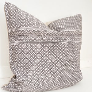 May include: A gray and white patterned throw pillow with a geometric design. The pillow is made of a soft, woven fabric.