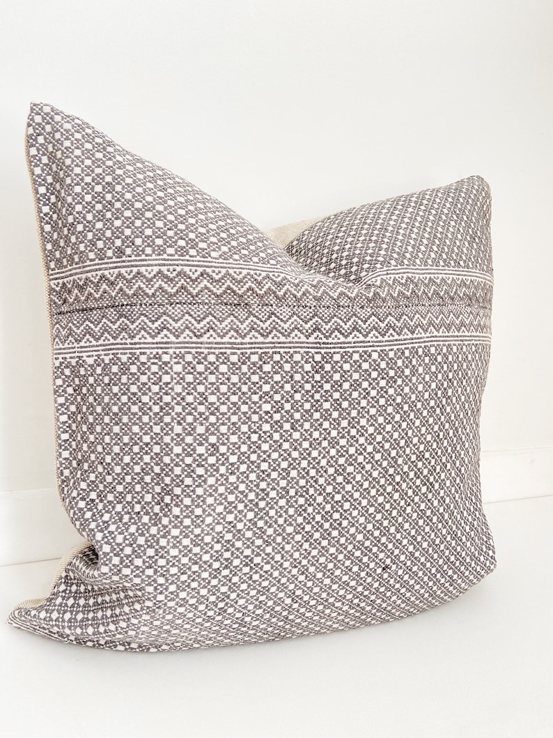 May include: A gray and white patterned throw pillow with a geometric design. The pillow is made of a soft, woven fabric.