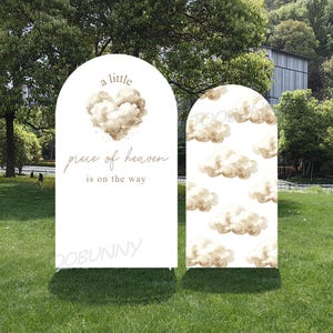 May include: Two white arched signs with a cloud theme. One sign has text that reads "a little piece of heaven is on the way" with a cloud heart. The other sign has a pattern of clouds.