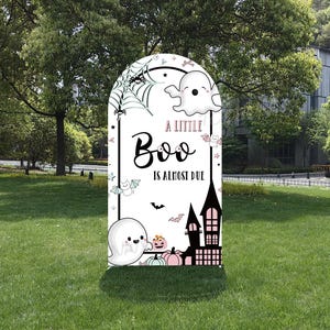 Może przedstawiać: Biały znak ogrodowy o tematyce Halloween w kształcie nagrobka. Znak przedstawia kreskówkowego ducha, nietoperze, pajęczynę i napis "A Little Boo Is Almost Due". Przedstawiono również czarny zamek i dynie.