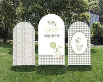 May include: Three outdoor party signs with a whimsical theme. The signs feature a light green and white color scheme, with a goose illustration and the text "Kolby is ONE silly goose". One sign has a gingham pattern.