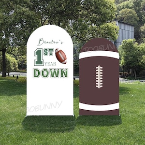 Op de afbeelding: Twee voetbal-thema tuinsignalen. Eén wit bord met de tekst "Braxton's 1st Year Down" met een voetbalafbeelding. Het andere bord is bruin met witte strepen en een voetbalvetersluiting. Beide borden staan op een groen gazon.