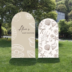 Könnte beinhalten: Zwei bogenförmige Babyparty-Schilder mit Muschel-Motiv. Ein Schild ist beige mit weißen Muschel-Illustrationen und dem Text "Alice's BABY SHOWER". Das andere Schild ist cremefarben mit braunen Muschel- und Schleifen-Illustrationen.