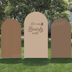Puede incluir: Tres paneles de fondo arqueados en tonos marrón y beige sobre hierba verde. El panel central tiene el texto "We can bearly wait" en una fuente cursiva. Los otros paneles tienen diseños decorativos.