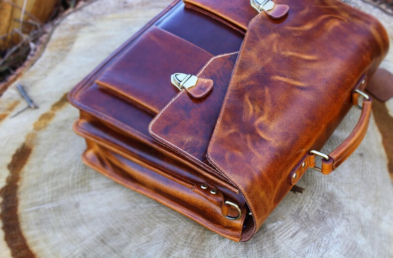 May include: A brown leather briefcase with a flap closure and a top handle. The briefcase has a distressed look and features brass hardware.