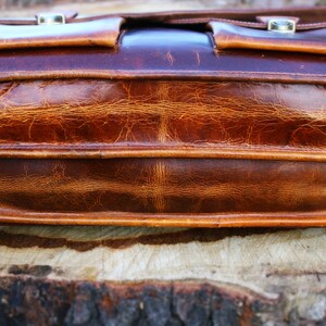 May include: A brown leather briefcase with two front pockets and a flap closure. The briefcase has a distressed look and is made of high-quality leather.