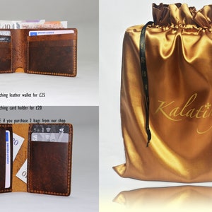 May include: A brown leather wallet with a stitched edge, open to reveal cash and cards. The wallet is displayed on a white surface. The image also shows a gold satin bag with black drawstrings and the text "Kalating" printed on the front.