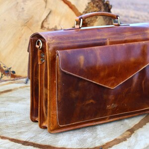 May include: A brown leather briefcase with a flap closure and a top handle. The briefcase has a worn, distressed look and is made of high-quality leather.