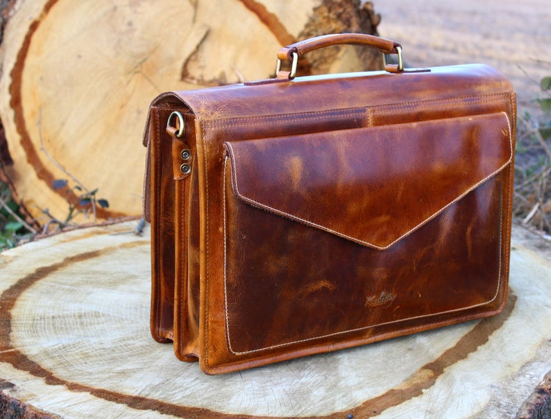 May include: A brown leather briefcase with a flap closure and a top handle. The briefcase has a worn, distressed look and is made of high-quality leather.