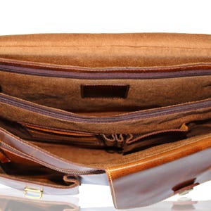 May include: A brown leather briefcase with multiple compartments and pockets. The interior is lined with a brown fabric. The briefcase has a zipper closure and a buckle.
