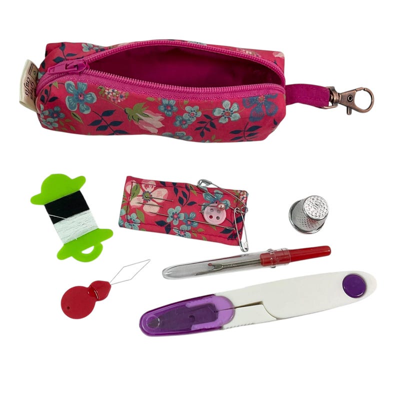 May include: A pink floral zippered pouch with a metal clip, containing a green thread spool with black and white thread, a floral needle cushion with pins, a silver thimble, a red needle threader, a seam ripper, and white and purple scissors.