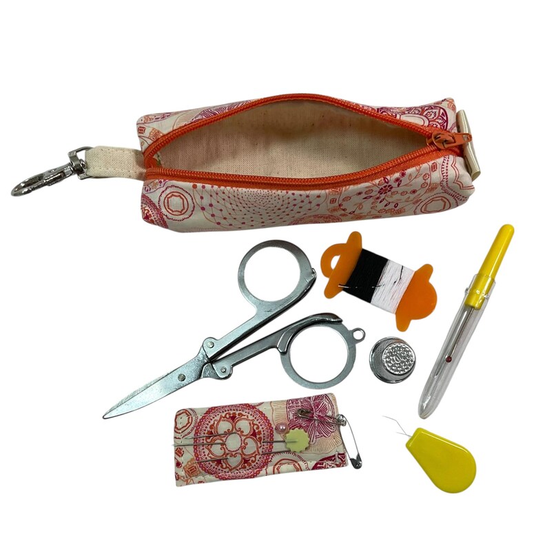 May include: A fabric pouch with a pink and orange circular pattern and an orange zipper, accompanied by metal scissors, a spool with black and white thread, a silver thimble, a yellow seam ripper, a yellow needle threader, and a small needle case.