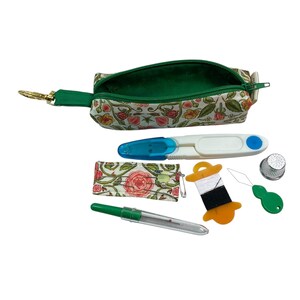 May include: A floral print fabric pouch with a green zipper and metal clip, containing sewing supplies: a white and blue seam ripper, a small needle case, a spool of black and white thread, a silver thimble, a green needle threader, and a seam gauge.