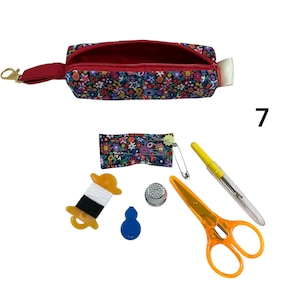 May include: A floral print fabric zipper pouch with a red interior and a gold lobster clasp. Included sewing accessories are a small floral pin cushion with a safety pin, a spool of white and black thread, a blue needle threader, a metal thimble, orange scissors, and a seam ripper.