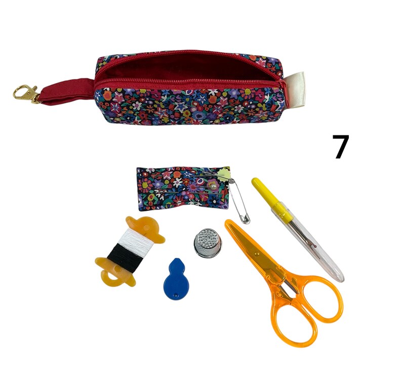 May include: A floral print fabric zipper pouch with a red interior and a gold lobster clasp. Included sewing accessories are a small floral pin cushion with a safety pin, a spool of white and black thread, a blue needle threader, a metal thimble, orange scissors, and a seam ripper.