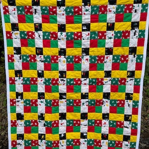 May include: A patchwork quilt with a checkered pattern in red, green, yellow, and black. The quilt is made of squares of different fabrics with various patterns, including white snowflakes and reindeer.