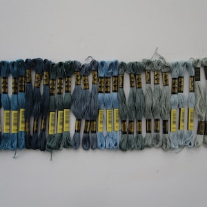 May include: A collection of 30 skeins of embroidery floss in shades of blue, gray, and white. The floss is arranged in a gradient from dark blue to light gray.