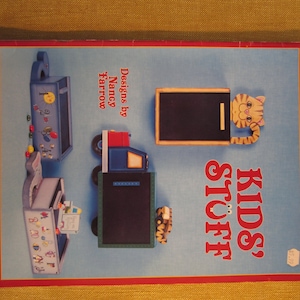 May include: A book cover with the title "Kids' Stuff" in red and white letters. The cover features illustrations of wooden toys, including a truck, a mailbox, and a toy with a chalkboard. The book is by Nancy Farrow.